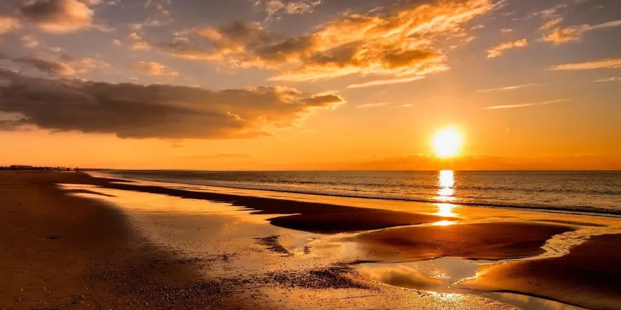 Golden sunset over a long sandy beach with tidal pools reflecting the sky