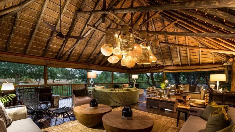 Luxury safari lodge interior with thatched roof, woven pendant lights, and open-air views of the bush